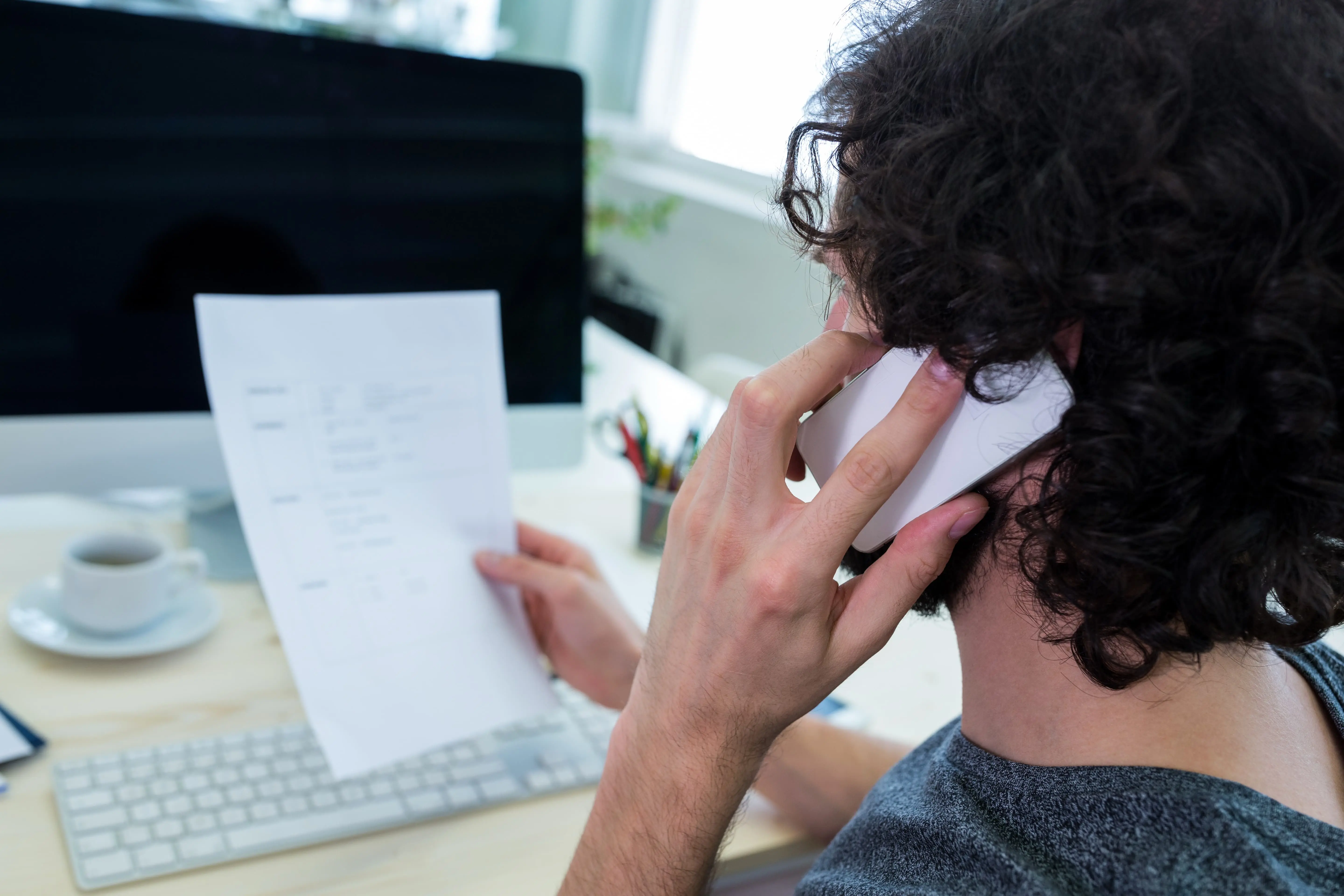 Representation d'une personne au telephone devant un pc avec un document a la main